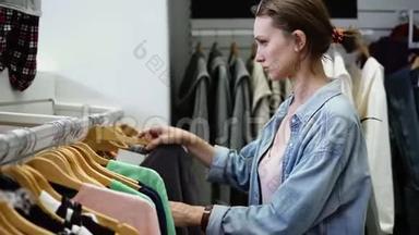 女孩正在寻找一个完美的衣服挂在一排在超市。 选择买什么。 购物守则